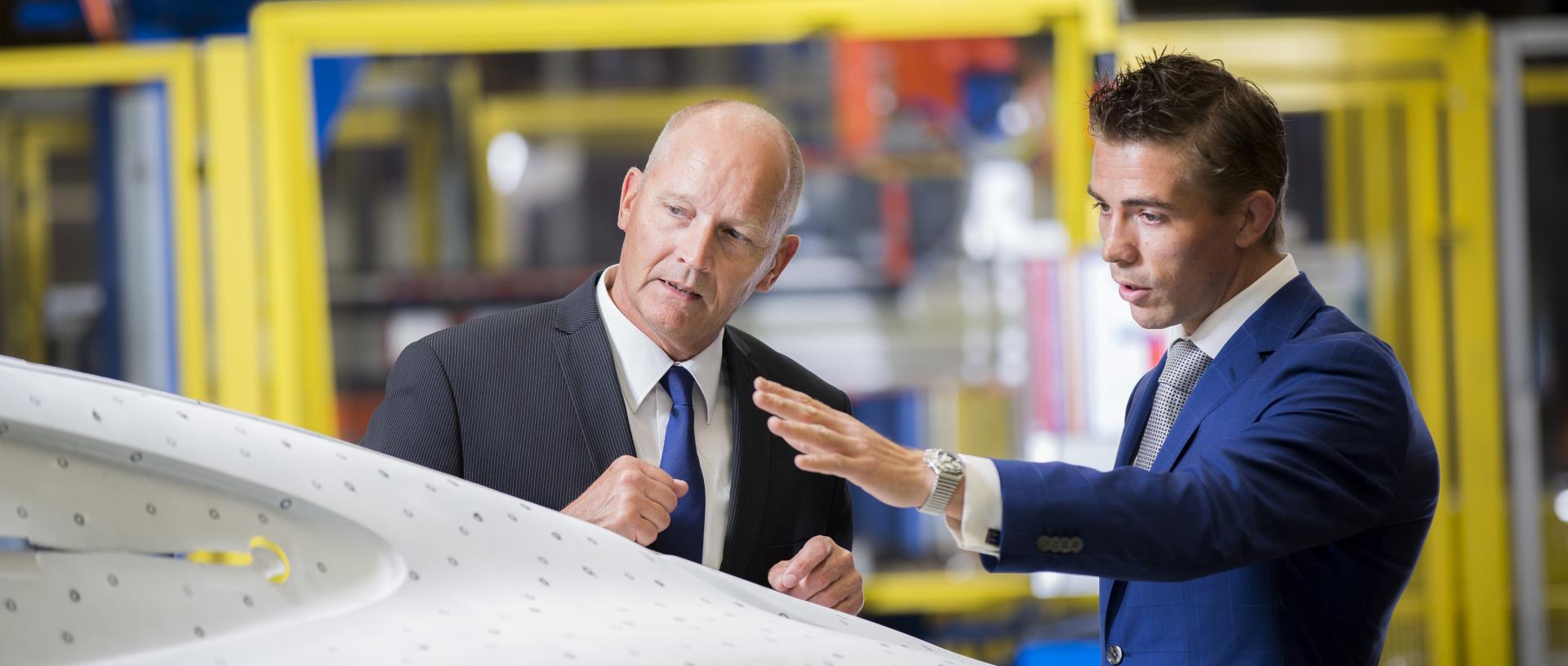Two business colleagues looking at a car panel, deep in discussion