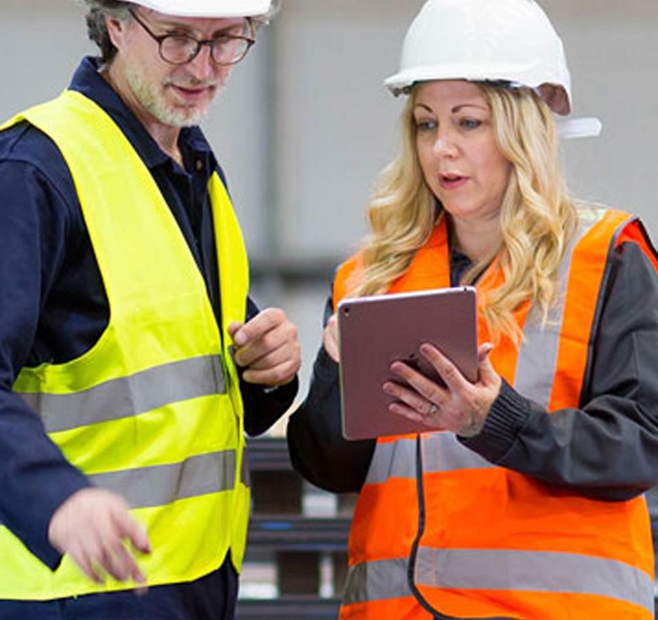 Man and woman wearing hard hats using mobile device for business