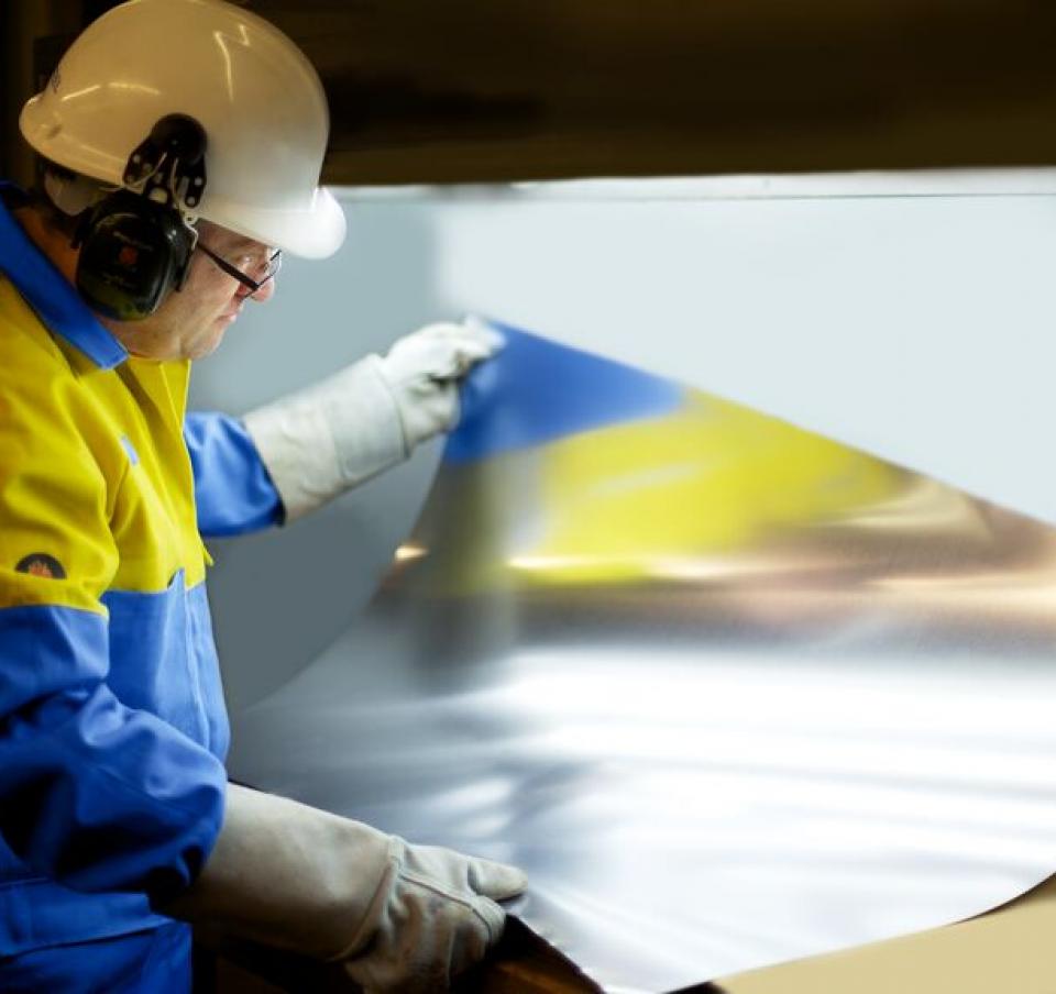 Packaging steel sheet being examined by Tata Steel employee wearing protective equipment