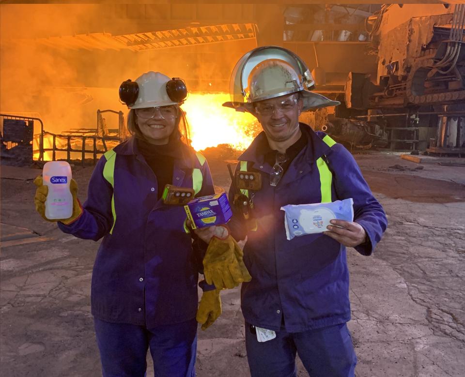Two steel workers in the forefront, holding sanitary products, with the steel making process in the background